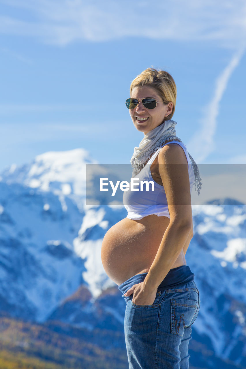 Portrait of smiling pregnant woman standing against mountains