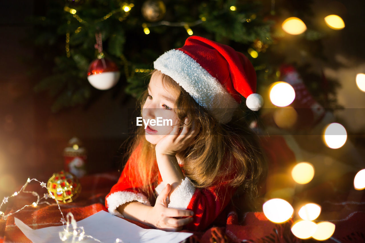 Cute girl lying down by illuminated christmas tree