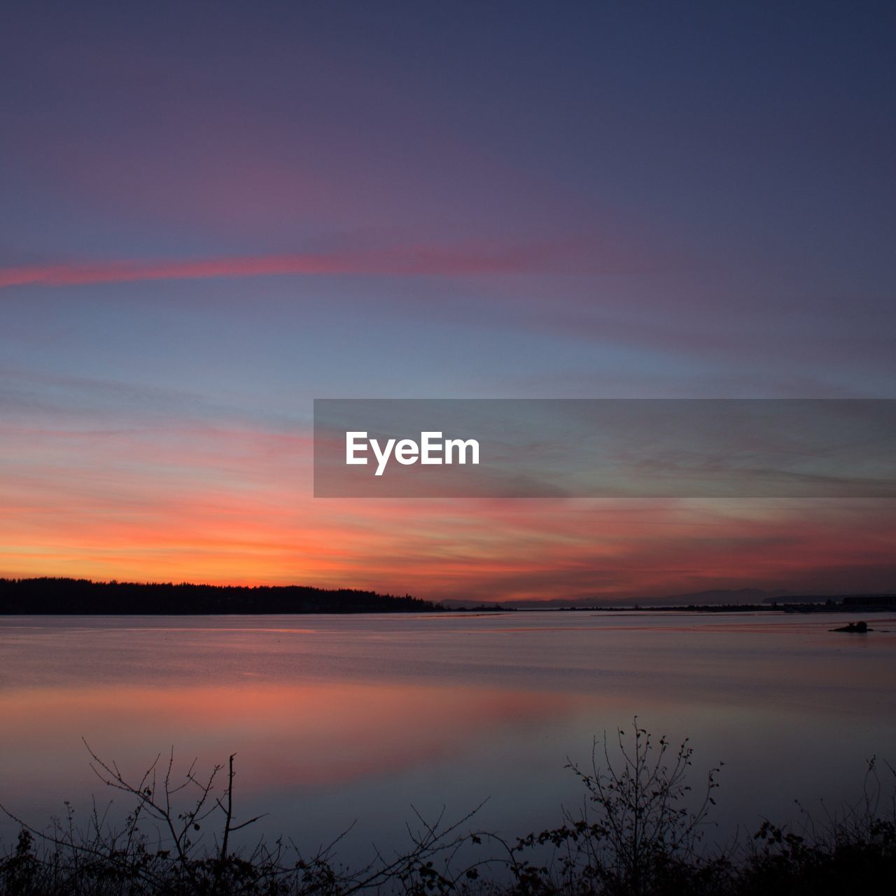 Scenic view of lake against cloudy sky at sunset