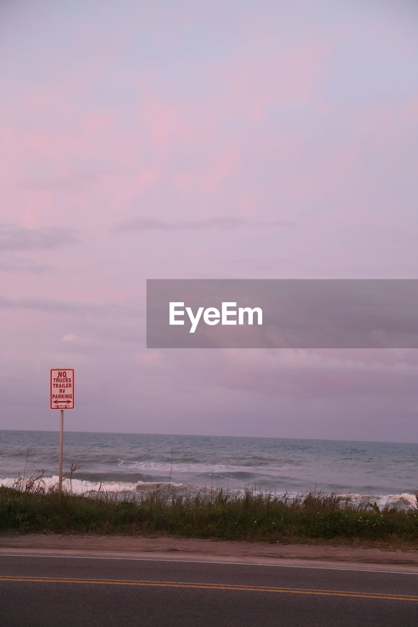 ROAD SIGN BY SEA AGAINST SKY