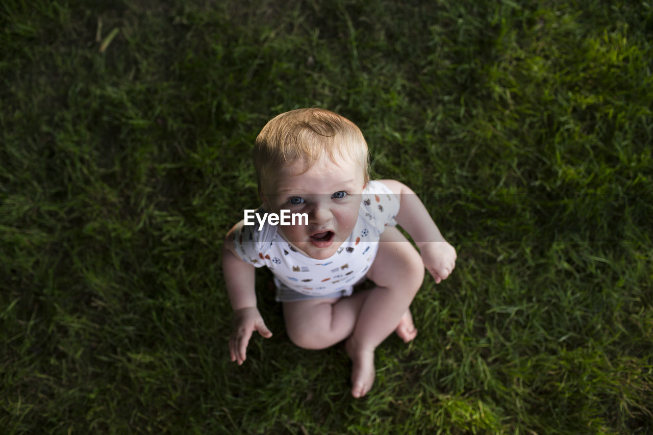 High angle portrait of cute baby boy sitting on grassy field at park