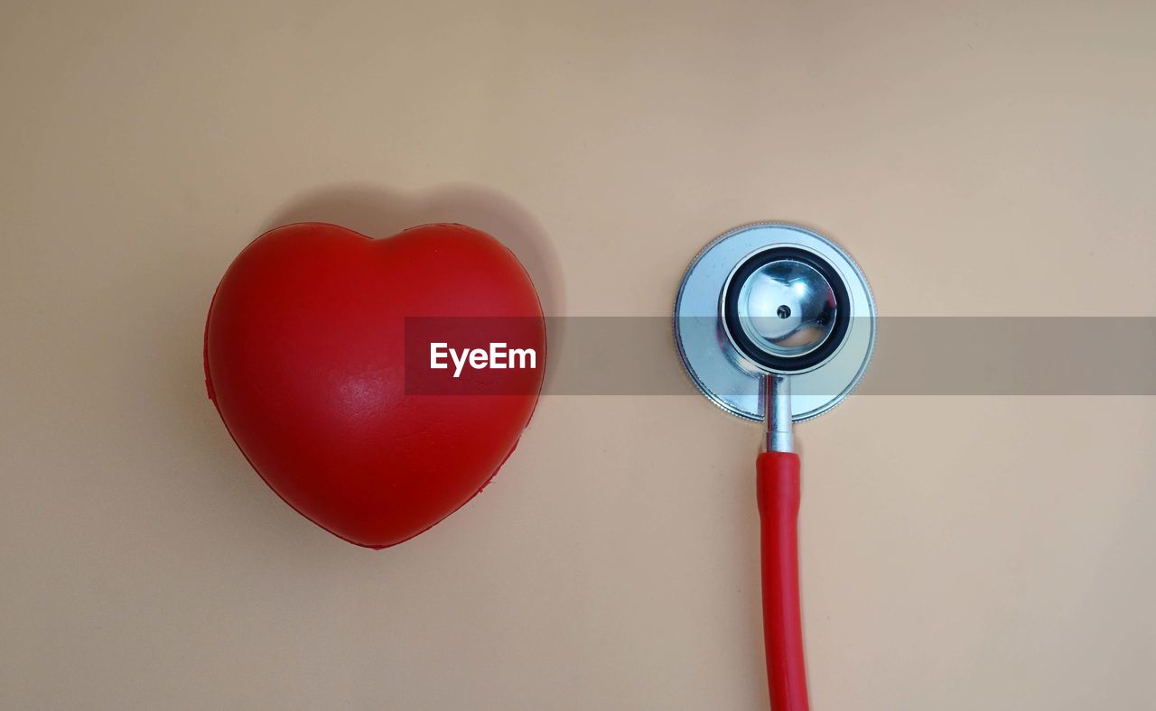Directly above shot of red heart model with stethoscope over white background