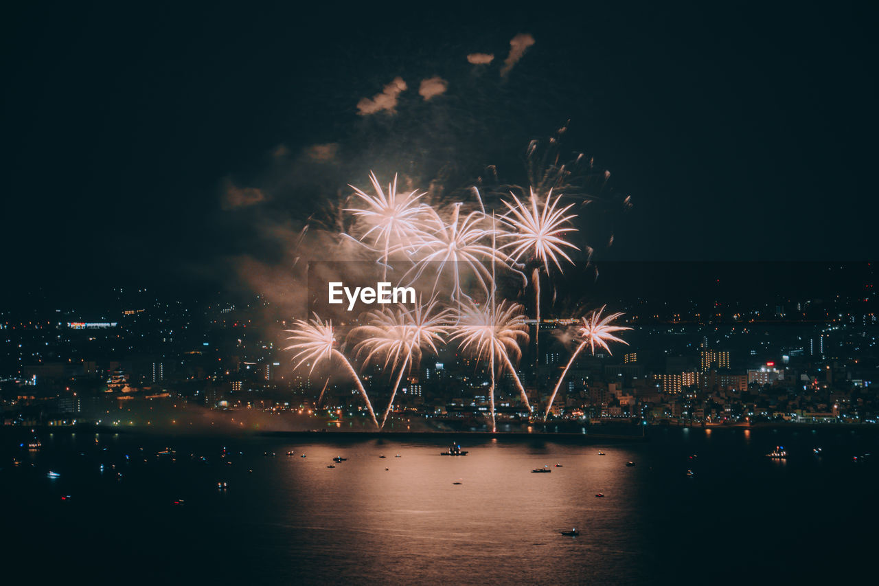 Firework display over illuminated city against sky at night