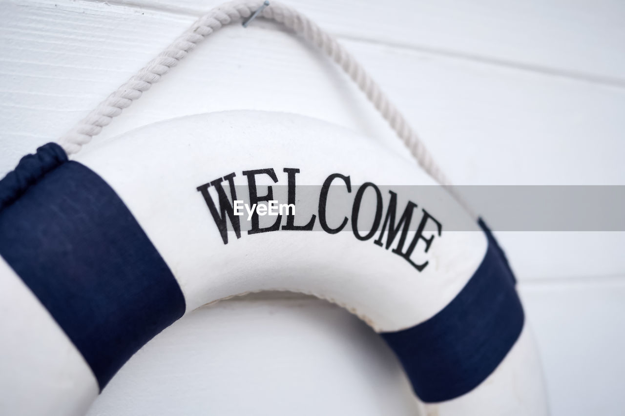 Close-up of welcome sign on life belt hanging on wooden wall