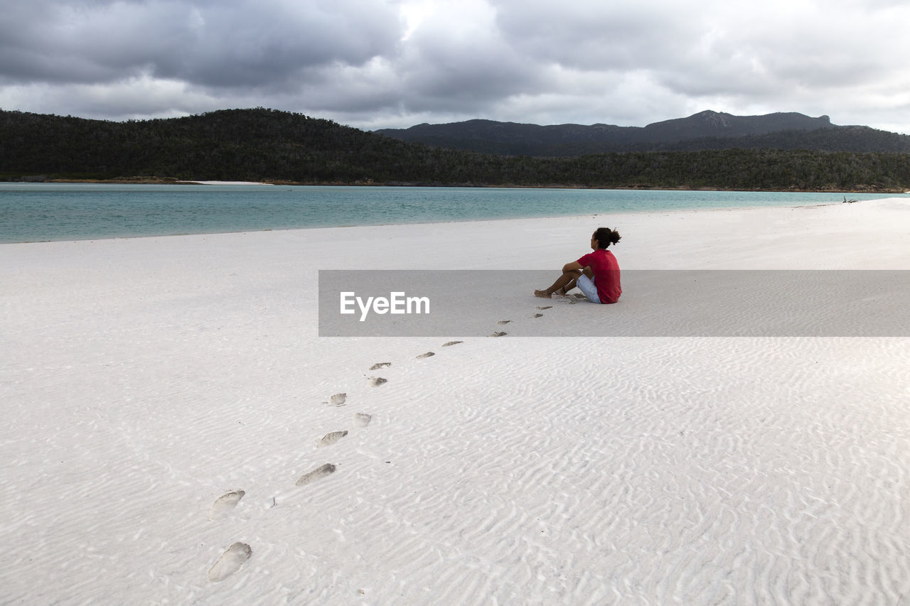 Tourist with man bun and red shirt at white sandy australian beach