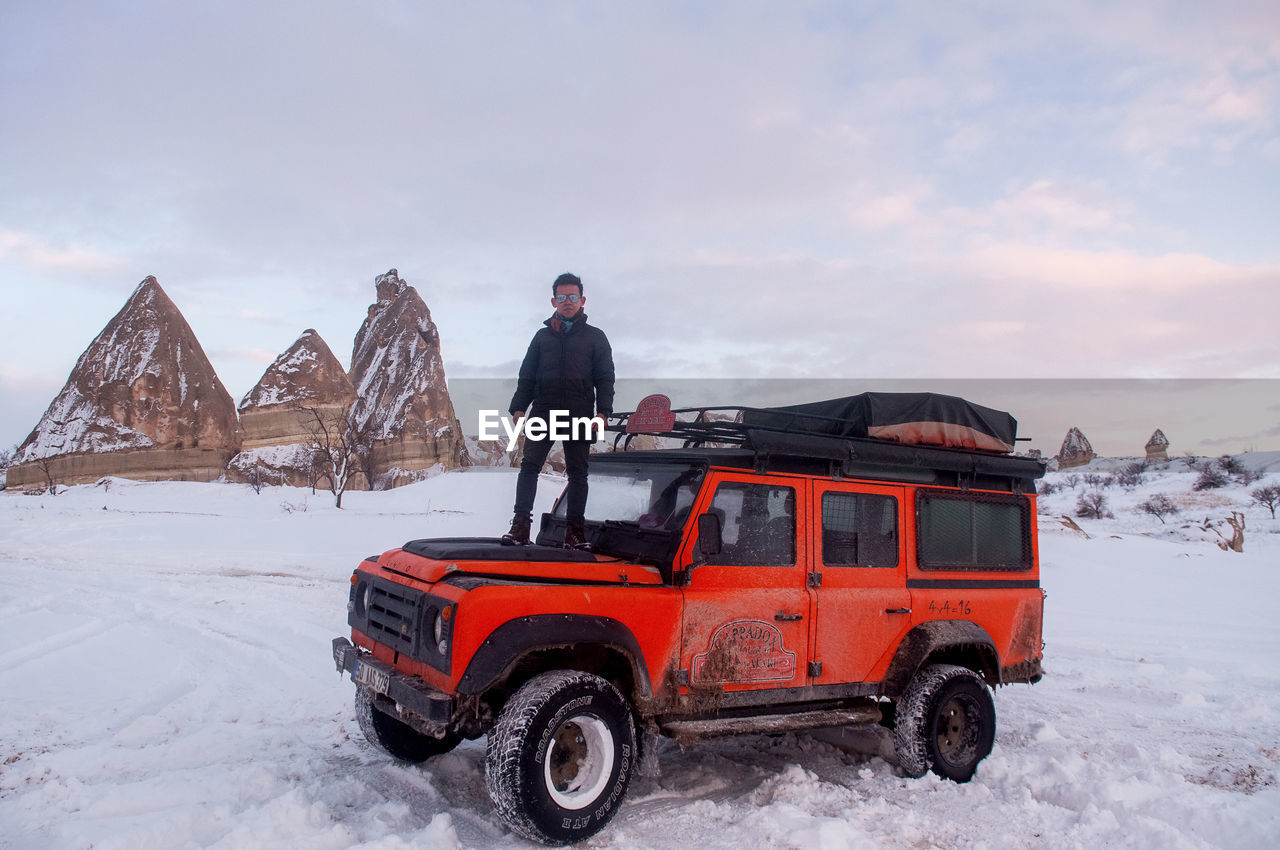 PEOPLE ON CAR AGAINST SNOWCAPPED MOUNTAIN