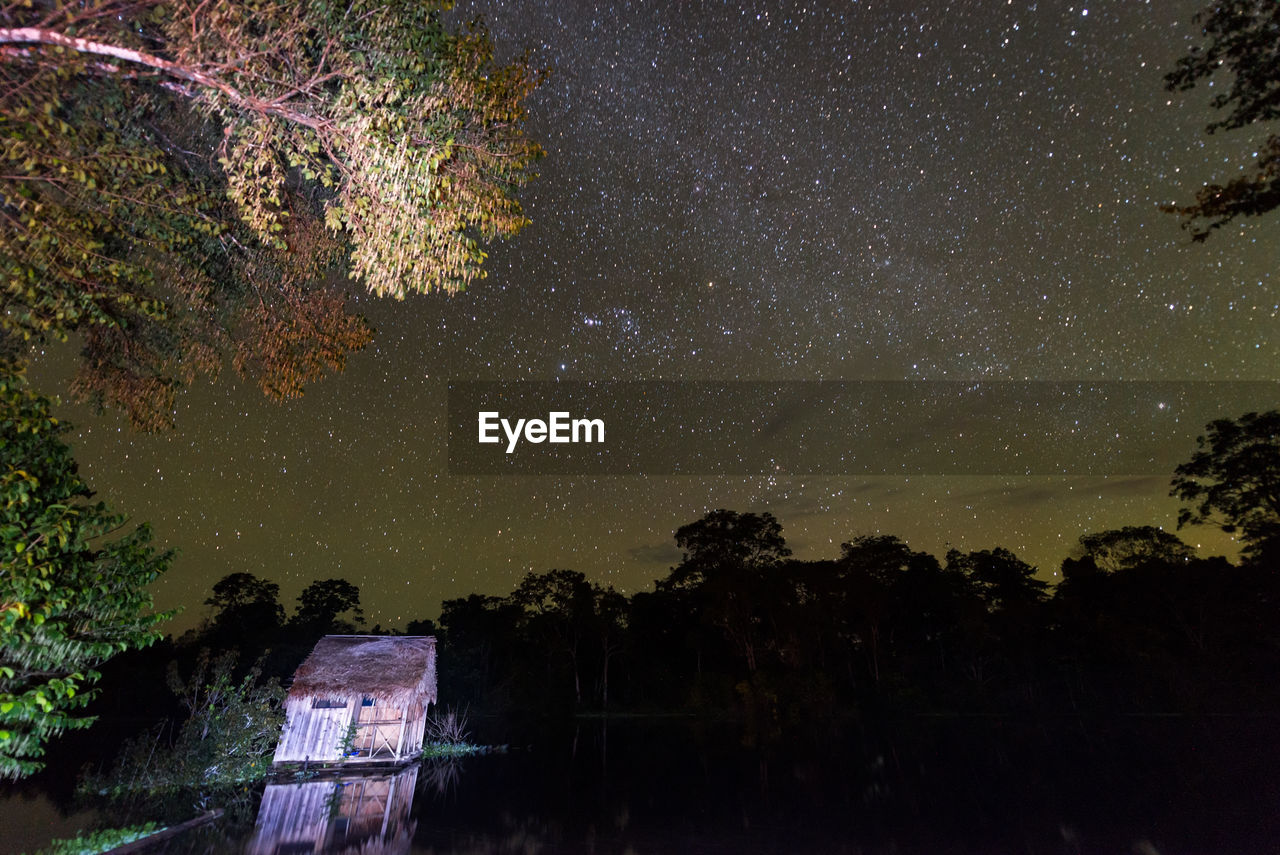 Hut by lake against star field