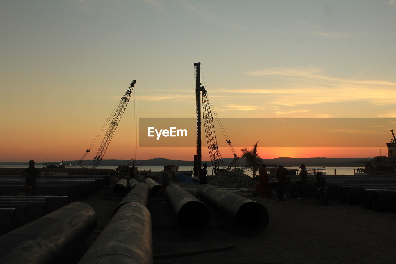 Construction site by sea against sky during sunset