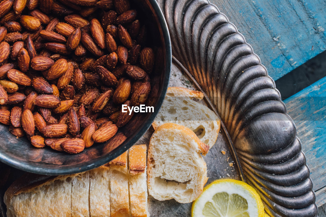 Picnic almonds in silver bowl on silver tray platter with bread, lemon on blue wood 