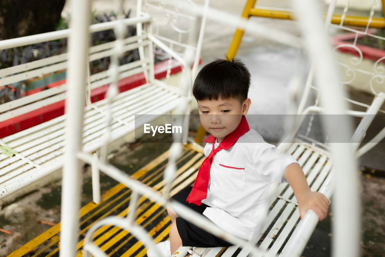 Cute boy playing while sitting on swing outdoors