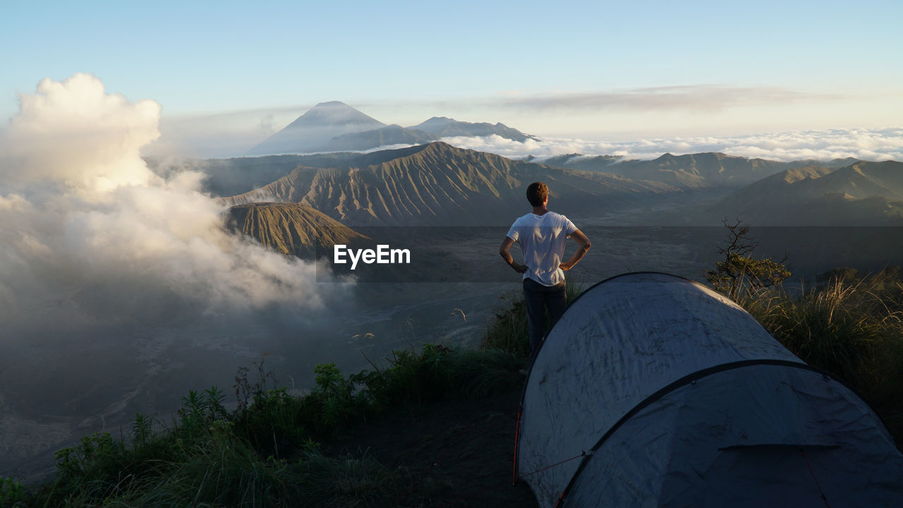 Rear view of man standing by tent on mountain against sky