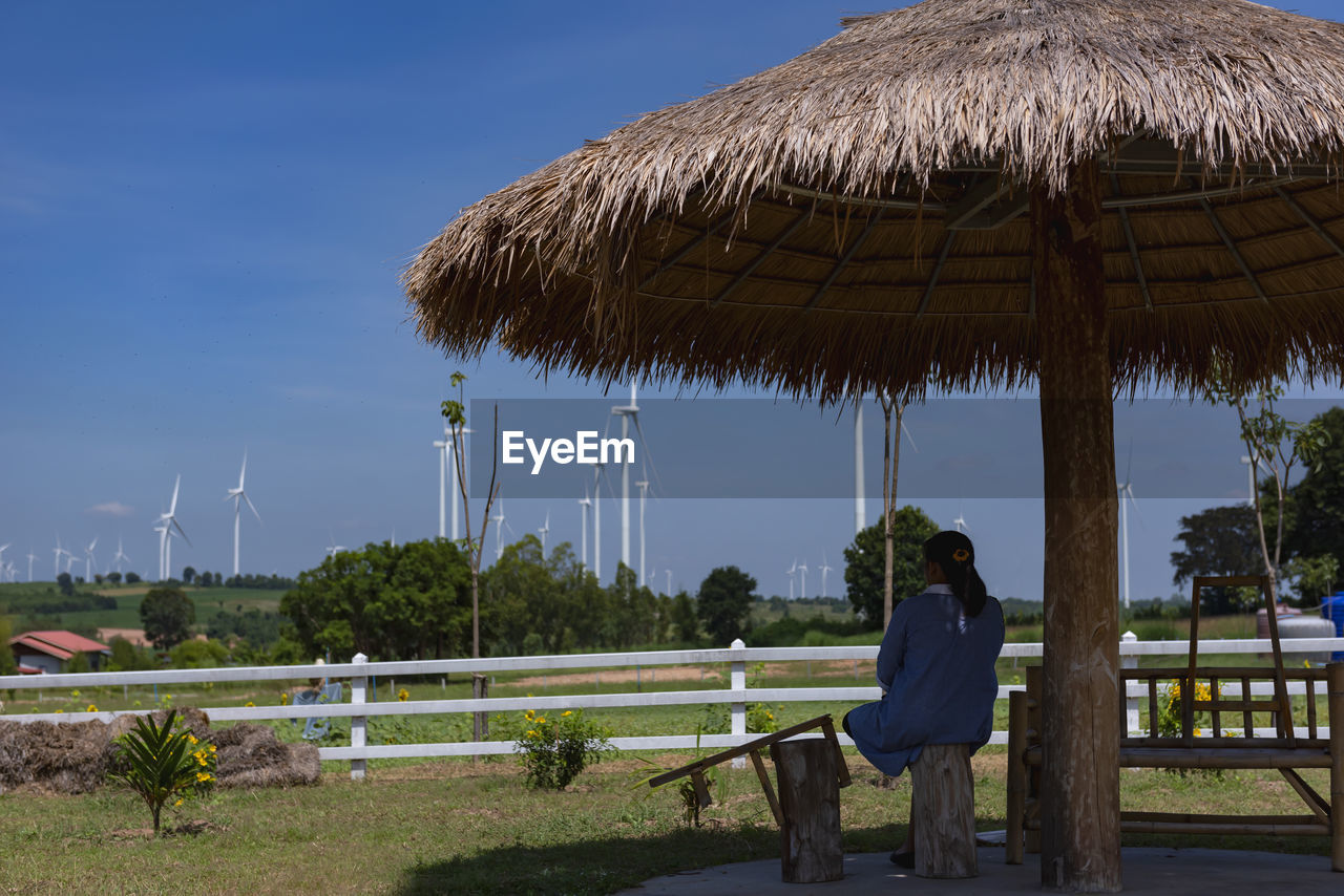 WOMAN SITTING ON ROOF AGAINST CLEAR SKY