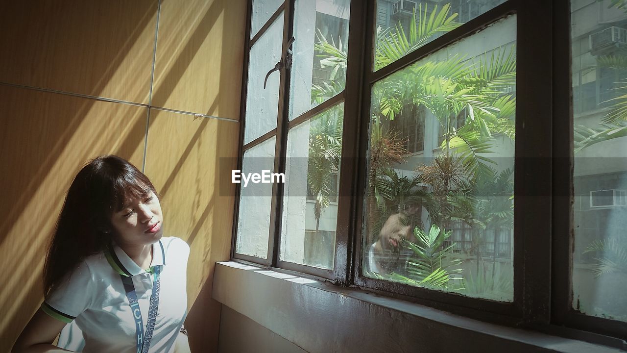 Young woman with eyes closed standing by window at home