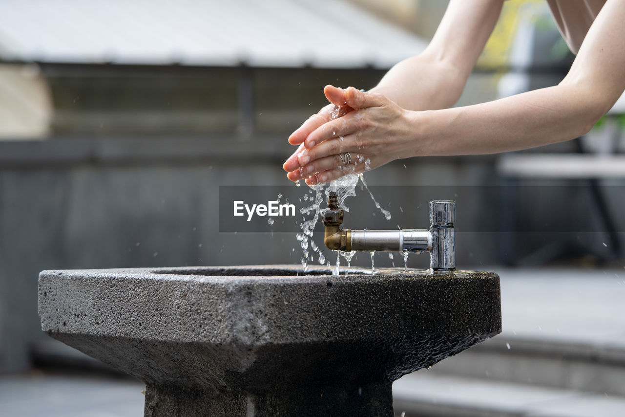 Hands with water pouring from tap in street. drops of water streaming up on fingers of young girl.