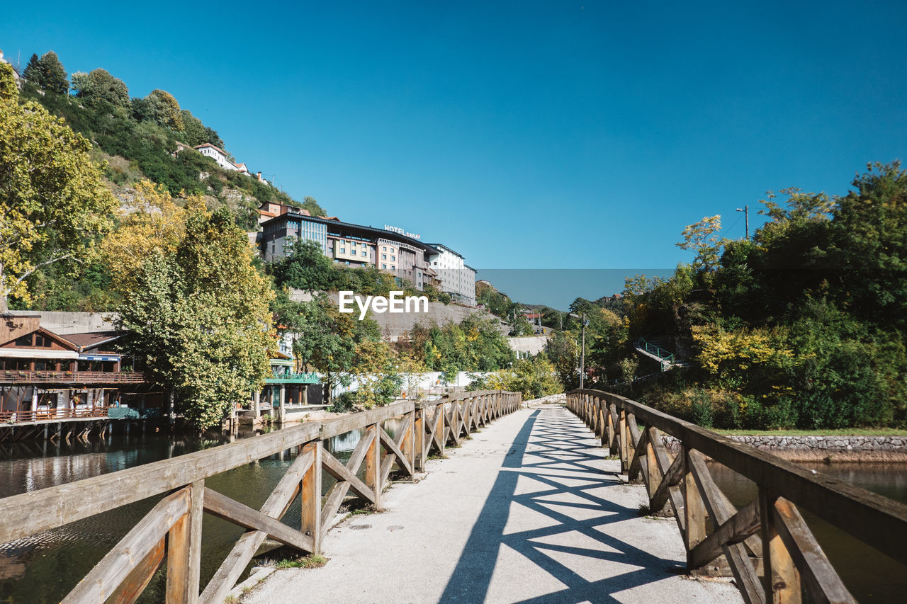 FOOTBRIDGE AMIDST TREES AGAINST BLUE SKY