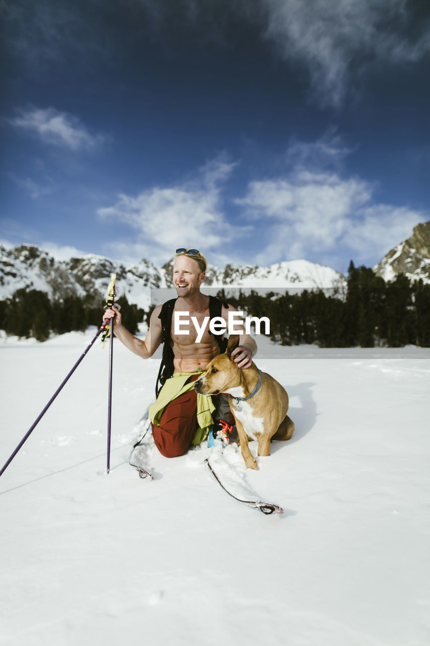 Cheerful hiker with dog on snowy field against mountains