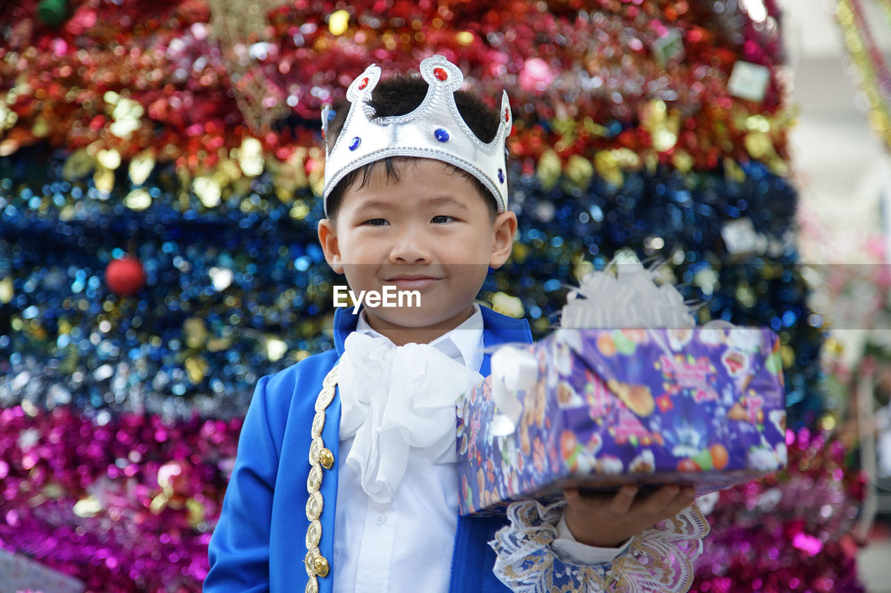 Smiling boy wearing crown holding gift box while standing in party