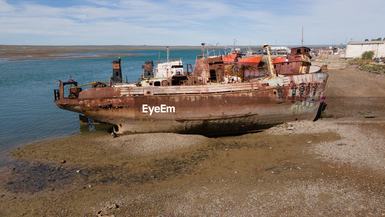 Abandoned boat moored on beach against sky