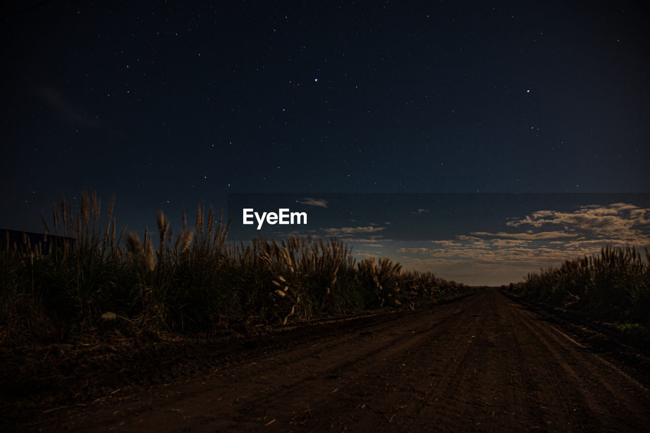 ROAD AMIDST FIELD AGAINST SKY AT NIGHT