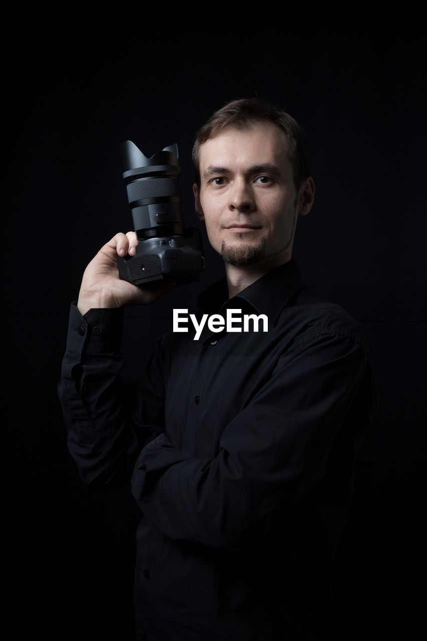 one person, portrait, adult, black background, studio shot, looking at camera, men, black, holding, weapon, gun, handgun, occupation, waist up, indoors, dark, darkness, camera, standing, person, young adult, serious, professional occupation, cut out, clothing, security, technology, front view, protection, aiming, activity