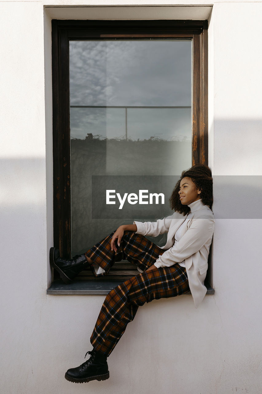 Thoughtful afro young woman sitting on window sill