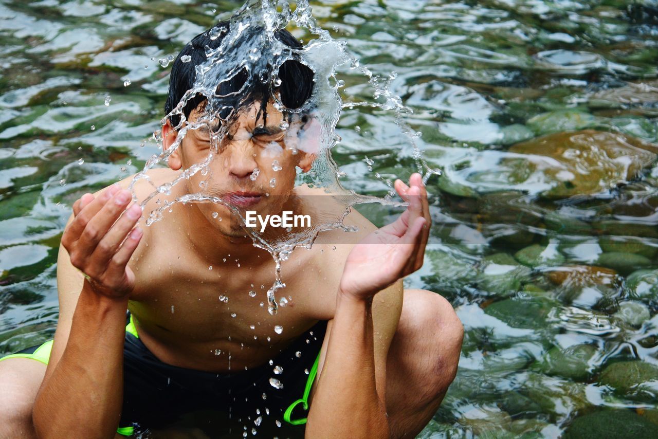 Shirtless man washing face in lake