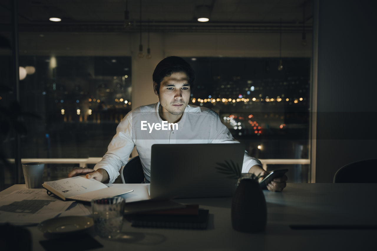 Determined businessman illuminated by laptop while working late in dark office