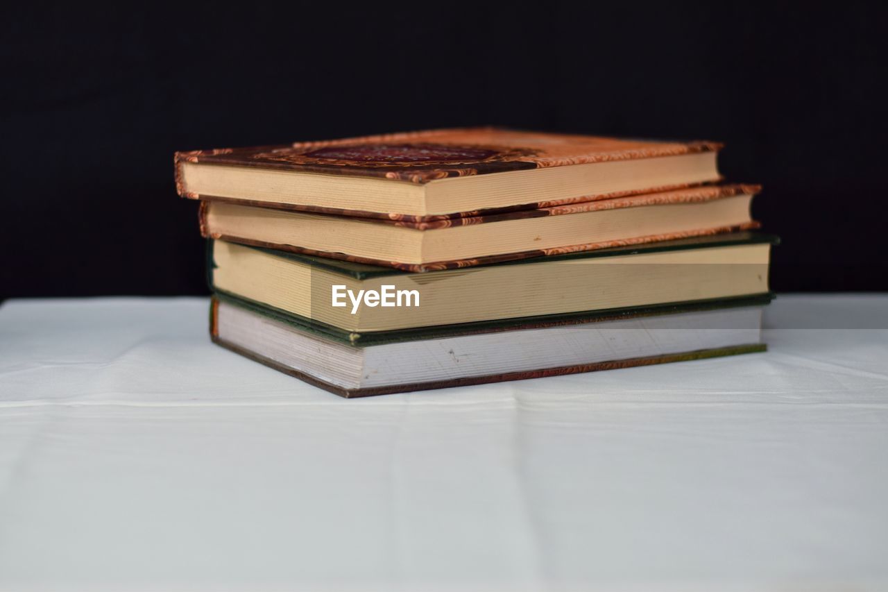 STACK OF BOOKS ON TABLE AGAINST BLACK BACKGROUND