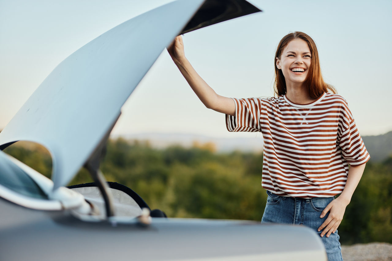 portrait of smiling young woman standing against car