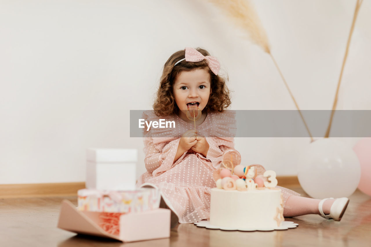 A cute little girl is sitting on the floor with a cake and gifts on her birthday.