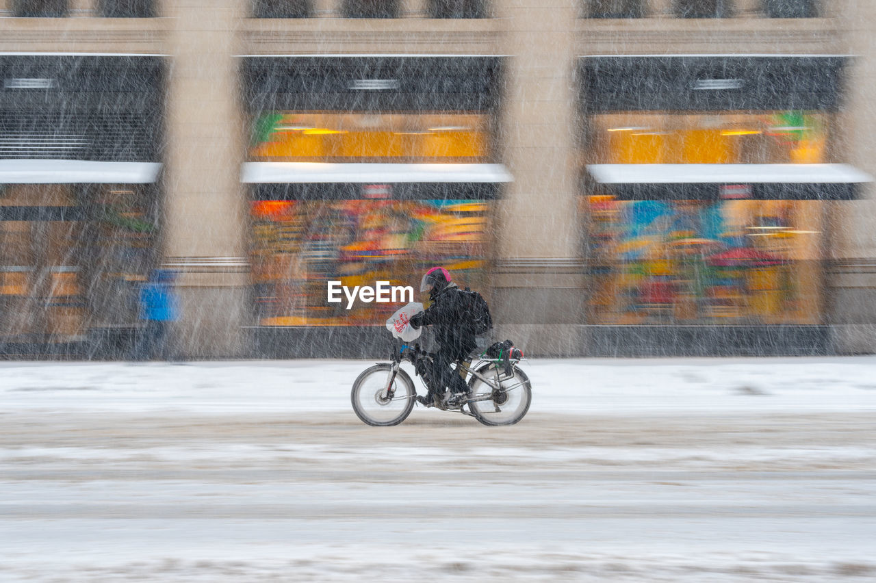 Man riding bicycle on street in city during snowstorm 