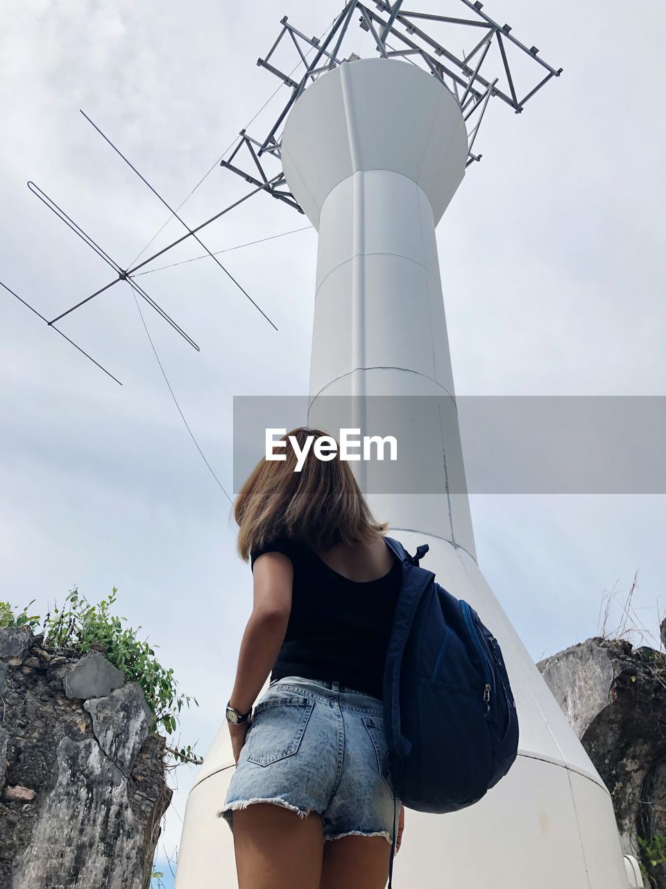 Low angle view of woman standing by communications tower against sky