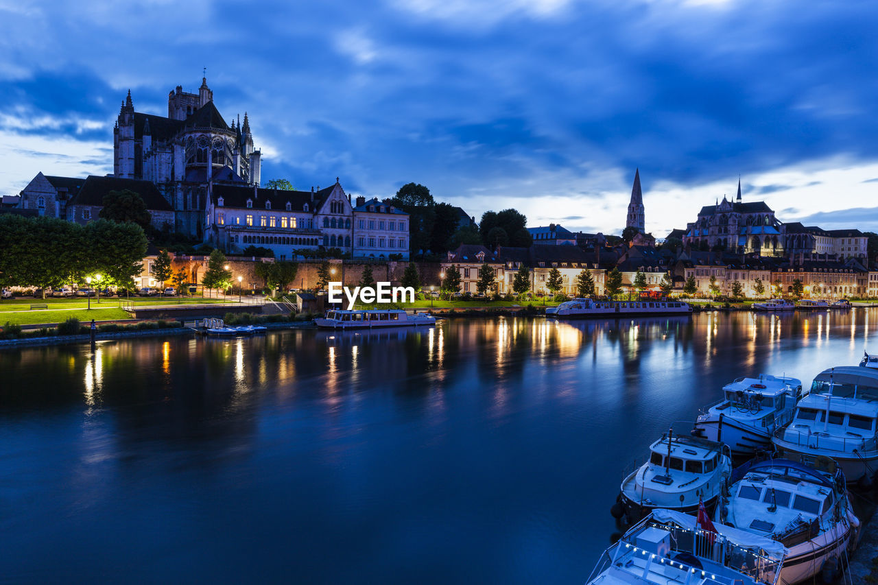 illuminated buildings by river against sky