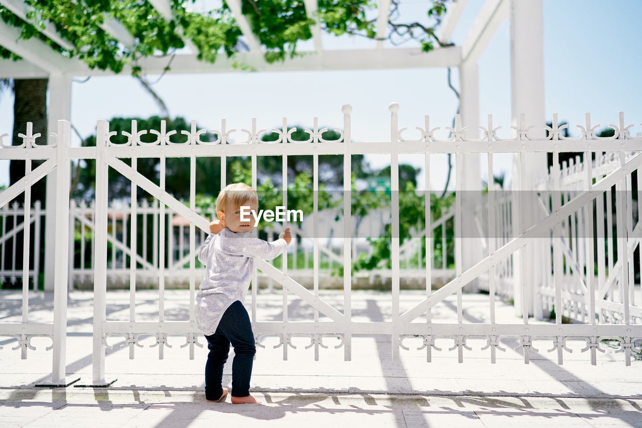 Boy standing by railing against fence