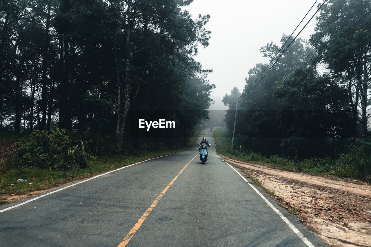 REAR VIEW OF WOMAN RIDING MOTORCYCLE ON ROAD