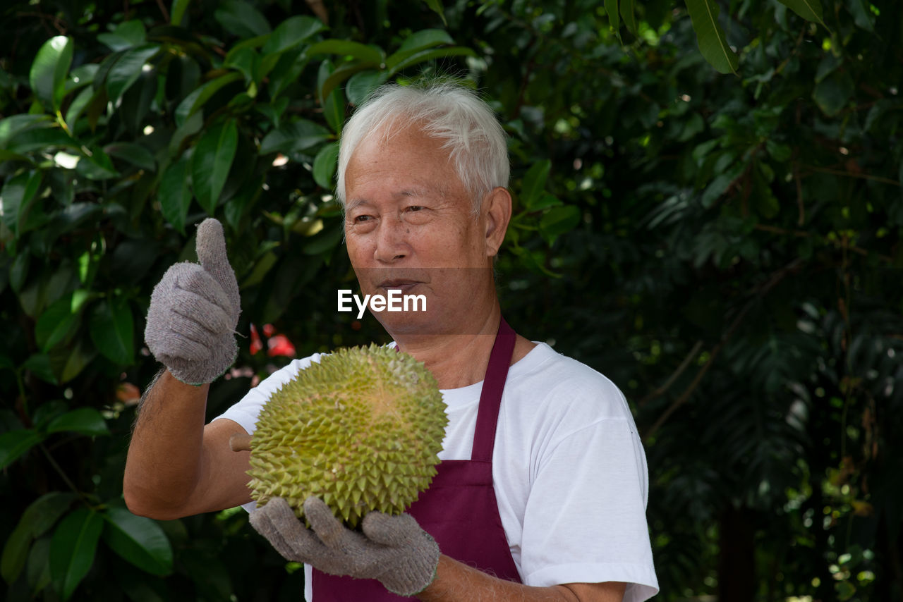 Smiling man showing thumbs up while holding durian