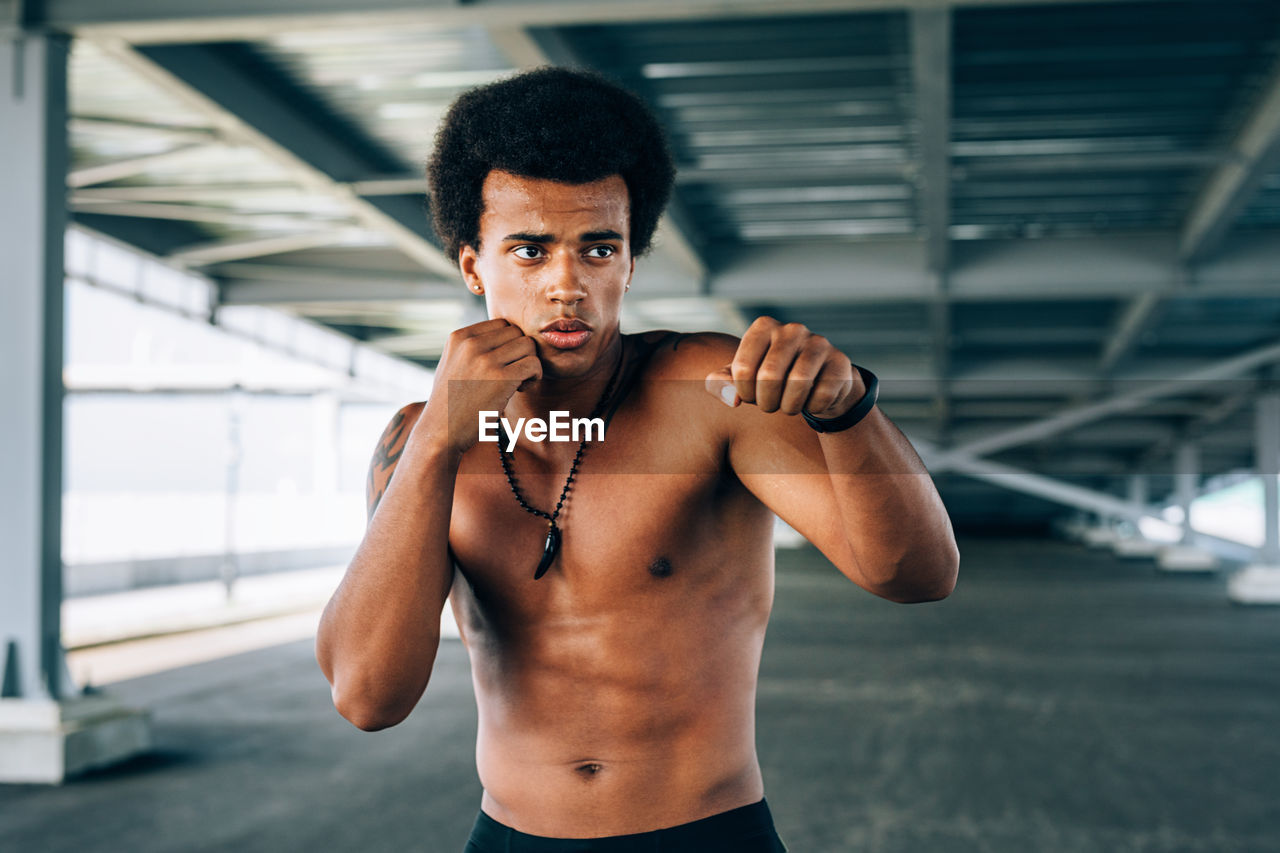 Shirtless male boxer exercising below bridge