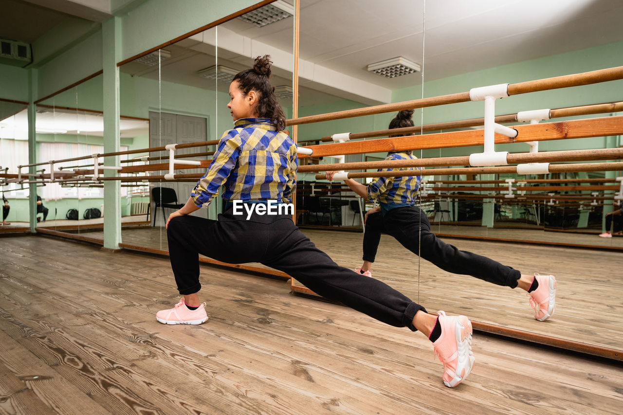 A young woman is engaged in contemporary dance alone in the choreography hall. back view