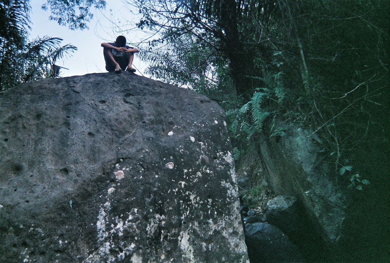 REAR VIEW OF MAN STANDING BY ROCK