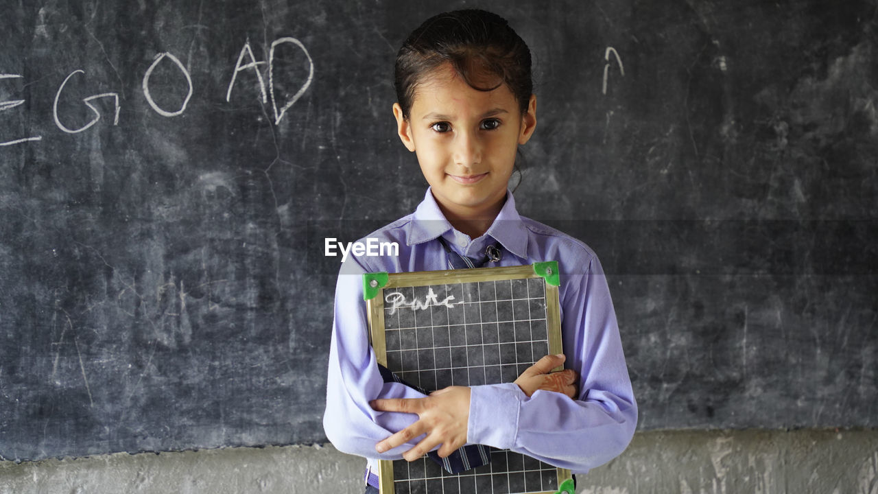 Portrait of happy cute little indian girl in school uniform holding blank slate