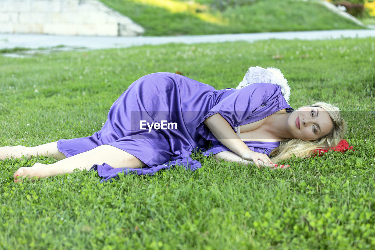 Beautiful blonde with long hair and long purple dress is balancing in public park. 