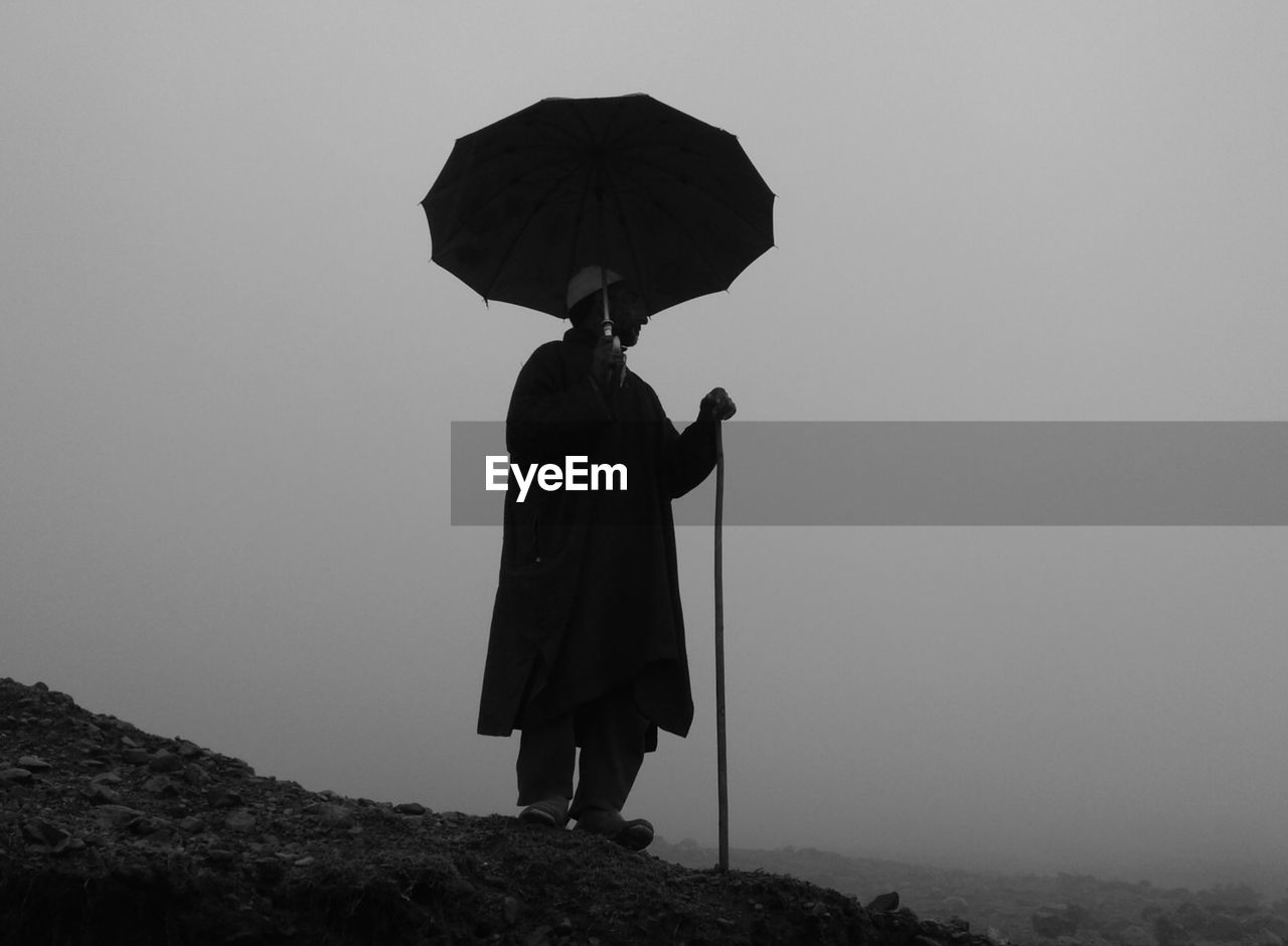 SILHOUETTE OF WOMAN HOLDING UMBRELLA AGAINST SKY