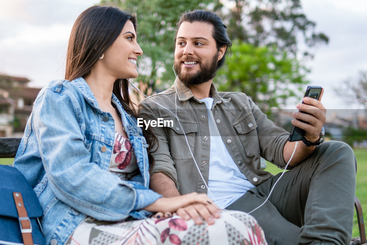 friends using mobile phone while sitting on sofa at park