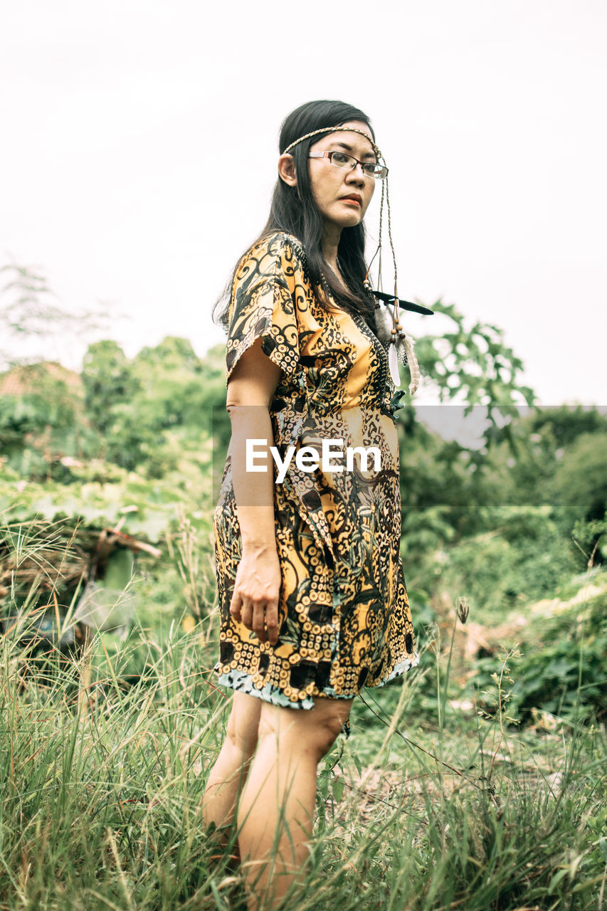 Young woman standing on field against sky