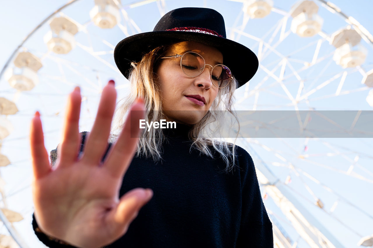 Low angle view of young woman wearing hat showing stop sign