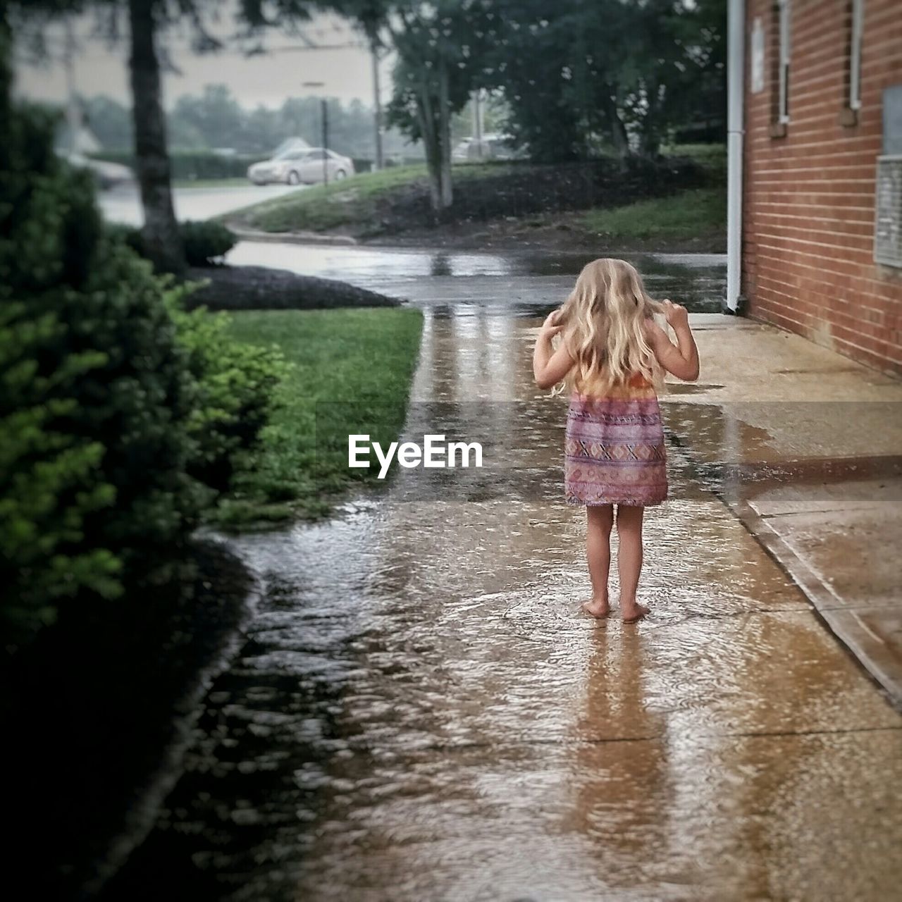 Rear view of girl playing in puddle on footpath