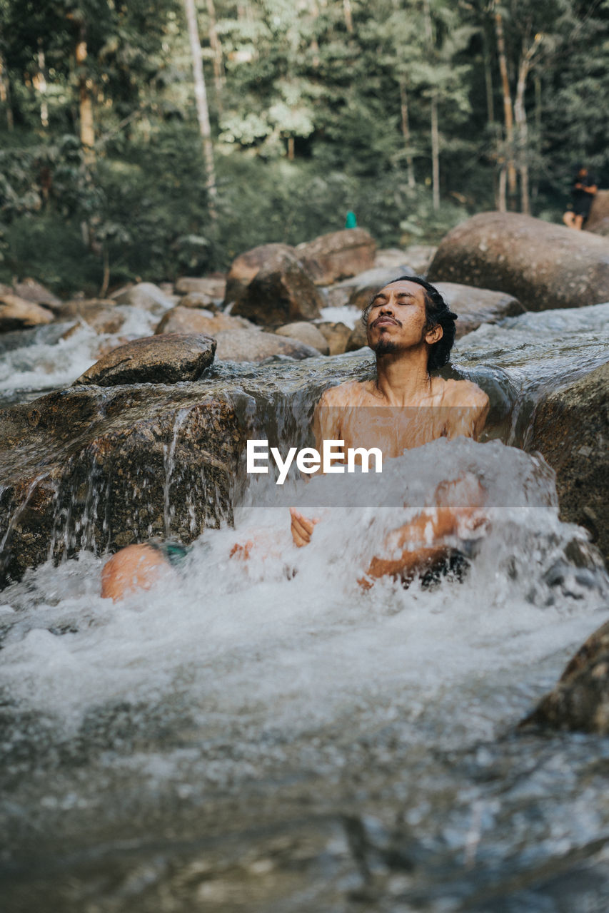 Shirtless man sitting on stream in forest