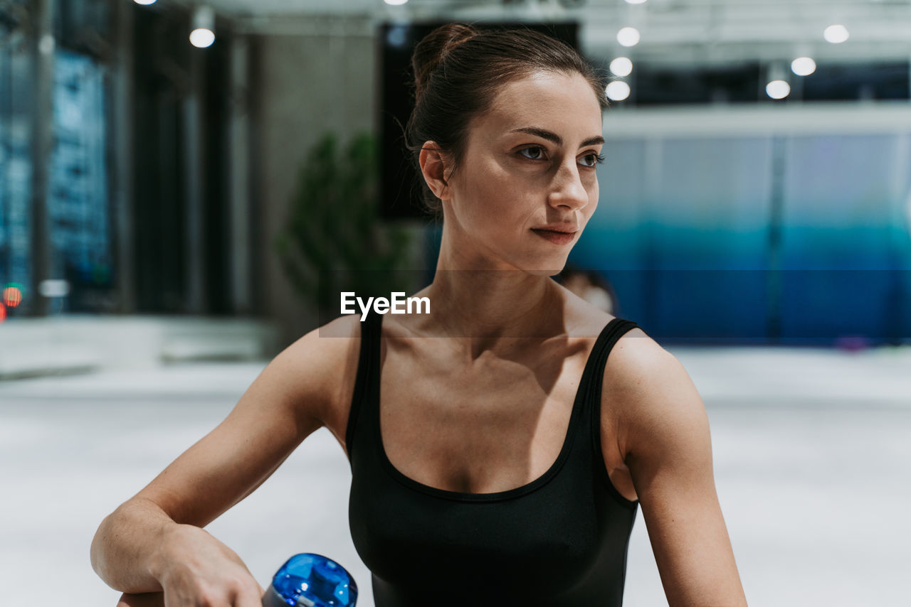 Smiling woman holding water bottle sitting at gym