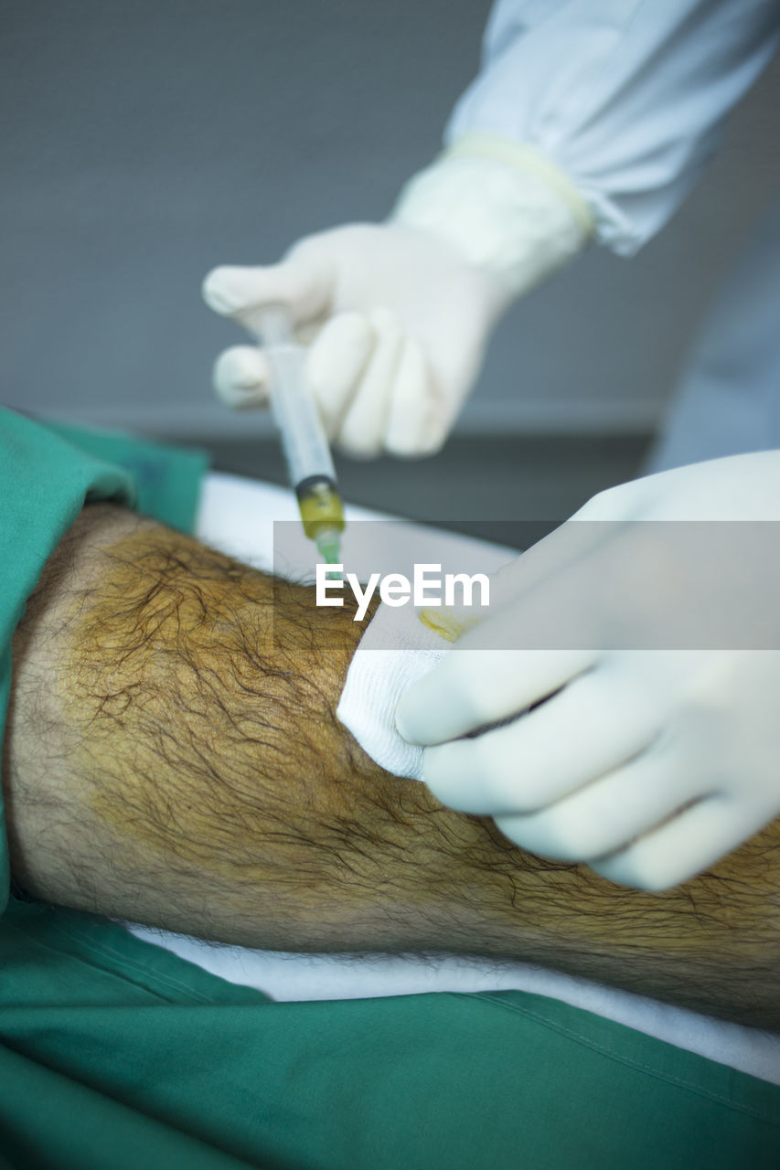 Cropped hand of surgeon injecting syringe in patient leg at hospital