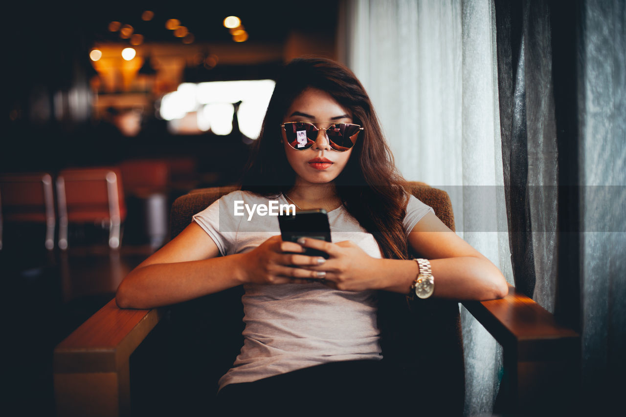 Young woman wearing sunglasses while using mobile phone at cafe